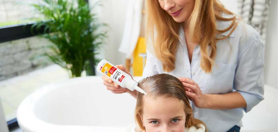 Ein Mädchen bekommt Ihre Haare mit mosquito Läuseprodukten von Ihrer Mutter behandelt