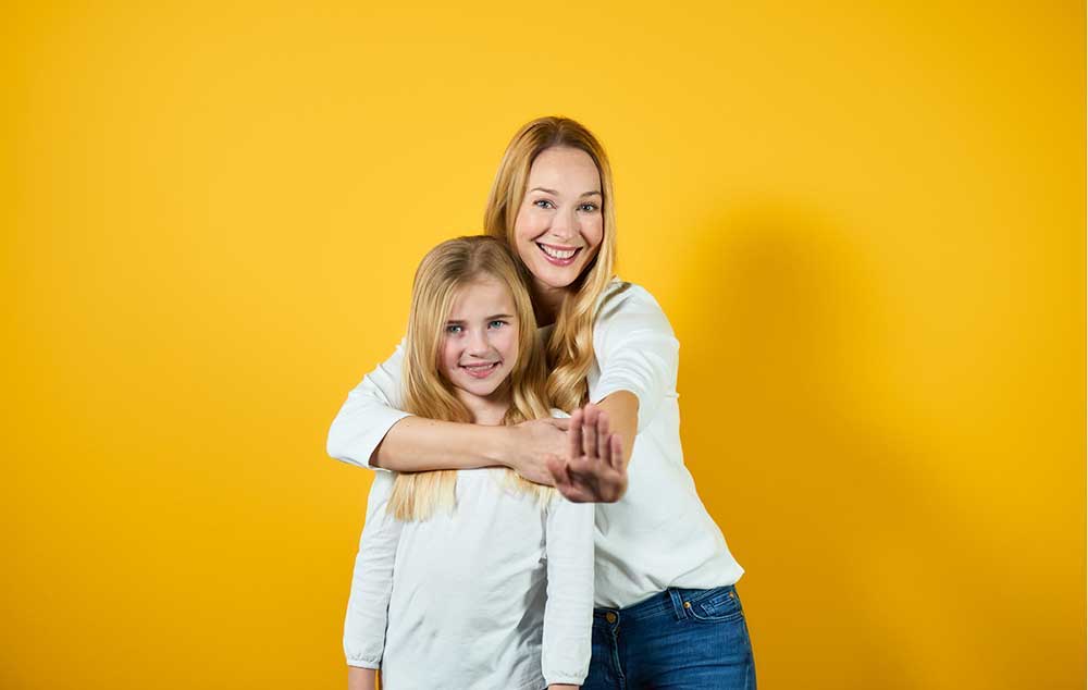 Eine Mutter umarmt Ihre Tochter und steht vor einem gelben Hintergrund